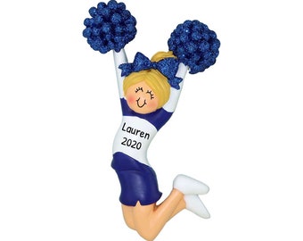 May include: A blue and white cheerleader ornament with pom-poms. The ornament has a smiling face and the name "Lauren 2020" written on the front.