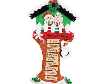 May include: A personalized Christmas tree ornament featuring a couple standing in front of a green birdhouse with a white picket fence. The tree trunk has a red banner that says "Merry Christmas" and a brown sign with the year "2021". The tree trunk also has several signs with names including Austin, Madison, Bradley, Benjamin, Jennifer, Heather, Gregory, Steven, and Michael.