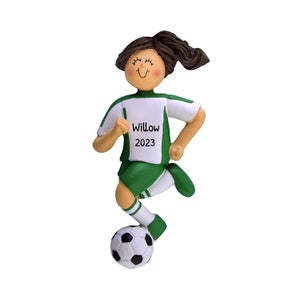 May include: Green and white soccer player ornament with brown hair, smiling, kicking a soccer ball. The ornament has the name "Willow" and the year "2023" printed on the front.