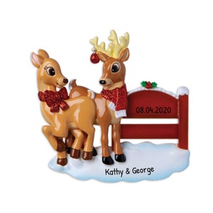 Puede incluir: Adorno navide&ntilde;o con dos renos con bufandas y lazos rojos. Los renos est&aacute;n frente a una valla roja con la fecha 08.04.2020. Los nombres "Kathy & George" est&aacute;n escritos en la base.