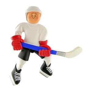 May include: A white hockey player ornament with a red and blue hockey stick. The player is wearing a white jersey, black shorts, and black skates with white laces. The player has a white helmet with a smiling face.