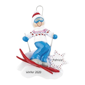 May include: A white ceramic Christmas ornament of a skier wearing a blue and white ski suit, a pink scarf, and a red and white hat. The skier is holding ski poles and is on red skis. The ornament has a white snowflake with red polka dots and the name "Patricia" written on it. The ornament also has the text "Winter 2020" on it.