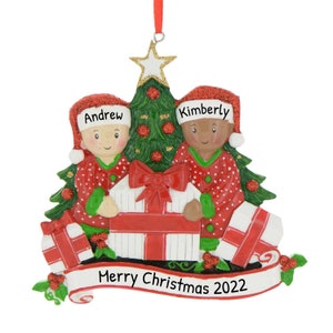 May include: Personalized Christmas ornament featuring two children in red pajamas holding presents in front of a green Christmas tree. The ornament has the names "Andrew" and "Kimberly" and the text "Merry Christmas 2022".