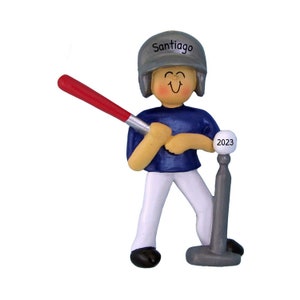 Könnte beinhalten: Ein personalisierter Baseball-Anhänger mit einer lächelnden Figur, die einen grauen Helm mit dem Namen "Santiago" trägt, ein blaues Trikot, eine weiße Hose und einen rot-weißen Schläger hält. Die Figur steht neben einem grauen Baseballständer mit dem Jahr "2023" darauf.