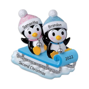 May include: A Christmas ornament featuring two penguins wearing hats and riding a sled. The penguins are named Samantha and Brandon. The sled has the text "Second Christmas" and "2022" on it.