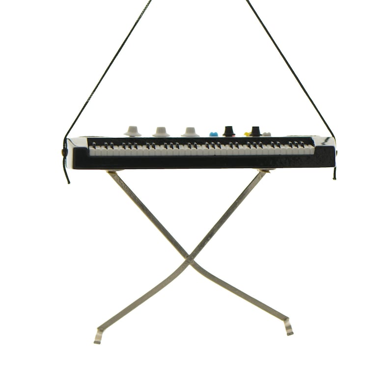 May include: A miniature black and white keyboard with several knobs and keys, suspended by a black string. The keyboard rests on a silver metal stand with an X-shaped design. The keys are white and black.