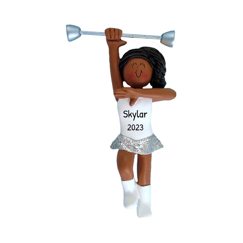 May include: A white and silver ornament of a girl twirling a baton. She is wearing a white leotard with a silver sequined skirt. The ornament has the name "Skylar" and the year "2023" on it.