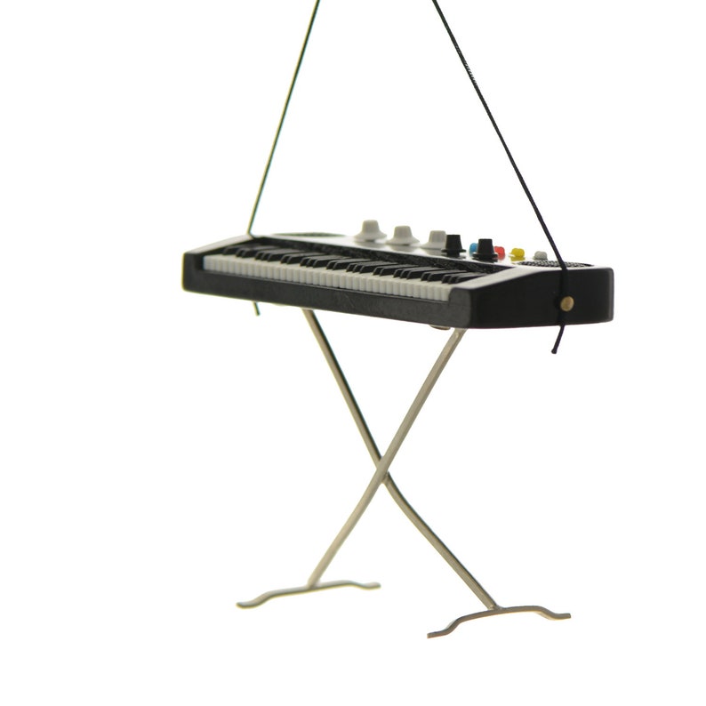 May include: Miniature black and white keyboard with a silver stand. The keyboard has white keys, black keys, and several knobs and buttons in various colors. The stand is made of silver metal and is in an X shape.