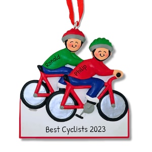 May include: Personalized Christmas ornament featuring two people riding bicycles, one in a red shirt and one in a green shirt. The ornament has the names "Ronald" and "Philip" and the text "Best Cyclists 2023".