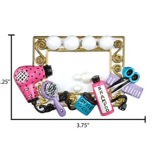 May include: A gold-colored picture frame with a white background and a variety of hair styling tools, including a pink hair dryer, a purple hairbrush, a bottle of shampoo, a bottle of styling gel, a pair of scissors, and a purple comb. The frame is 3.75 inches wide and 2.25 inches tall.