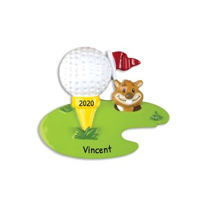 May include: A golf-themed ornament featuring a white golf ball on a yellow tee with the year "2020" printed on it. A smiling cartoon gopher and a red flag are also present. The name "Vincent" is printed on the green base.