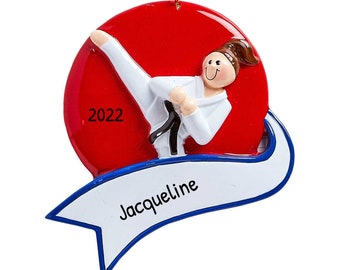 May include: Ornament featuring a figure in a white karate uniform performing a high kick against a red backdrop. A white banner with blue trim displays the name "Jacqueline". The year "2022" is printed on the red background.