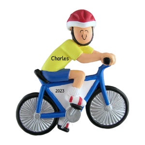 May include: A figurine of a person riding a blue bicycle, wearing a yellow shirt, blue shorts, and a red helmet. The name "Charles" is printed on the shirt, and the year "2023" is printed on the bicycle.