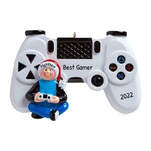 Könnte beinhalten: Weißer und schwarzer Videospiel-Controller-Weihnachtsbaumschmuck mit einer kleinen Figur eines Menschen, der einen Weihnachtsmann-Hut trägt und einen Videospiel-Controller hält. Der Anhänger trägt die Aufschrift "Best Gamer" und "2022".