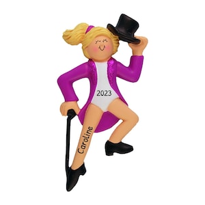 May include: A personalized Christmas ornament featuring a girl in a purple jacket and white leotard, holding a cane and wearing a black top hat. The ornament is decorated with glitter and the text "2023" and "Caroline".