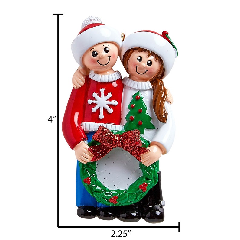 Puede incluir: Un adorno navide&ntilde;o personalizado que representa a una pareja con su&eacute;teres rojos y blancos con un copo de nieve y un dise&ntilde;o de &aacute;rbol de Navidad. Est&aacute;n sosteniendo una corona verde con un lazo rojo y un espacio en blanco para una foto. El adorno mide 10 cm de alto y 5,7 cm de ancho.