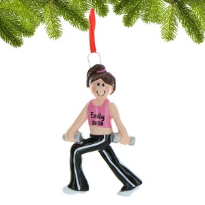 Pu&ograve; includere: Un ornamento natalizio personalizzato con una donna dei cartoni animati che indossa pantaloni neri e una canotta rosa, tenendo in mano dei manubri. L'ornamento ha il nome "Emily" e l'anno "2018" scritto su di esso.