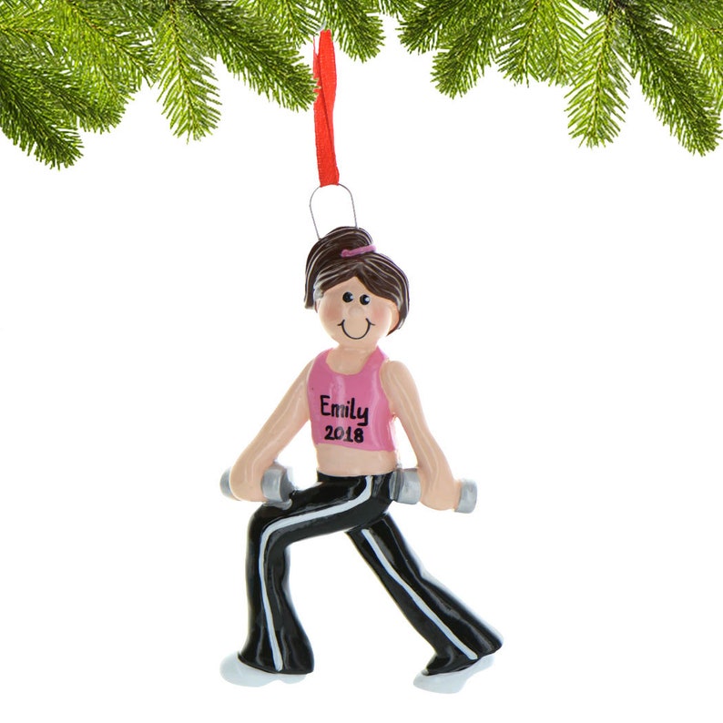 Pu&ograve; includere: Un ornamento natalizio personalizzato con una donna dei cartoni animati che indossa pantaloni neri e una canotta rosa, tenendo in mano dei manubri. L'ornamento ha il nome "Emily" e l'anno "2018" scritto su di esso.