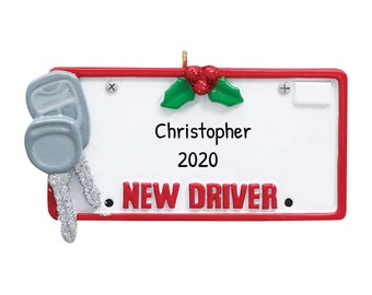 Può includere: Un ornamento rettangolare con bordo rosso e le parole "NEW DRIVER" in rosso. L'ornamento ha uno sfondo bianco con il nome "Christopher" e l'anno "2020" in nero. Un set di chiavi dell'auto grigie con accenti glitterati argentati è a sinistra.