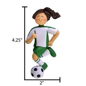 May include: Green and white soccer player ornament with brown hair, smiling, kicking a black and white soccer ball. The ornament is 4.25 inches tall and 2 inches wide.