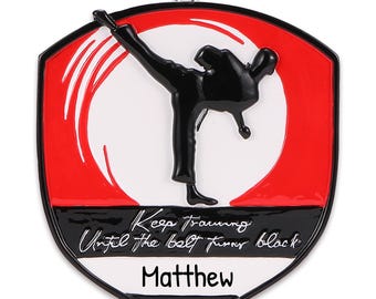 May include: A red and white shield-shaped Christmas ornament with a black silhouette of a person doing a martial arts kick. The ornament has the text "Keep training until the belt turns black" and the name "Matthew".