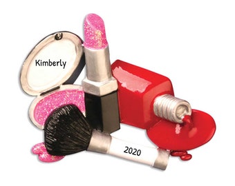 Könnte beinhalten: Ein Make-up-Ornament mit einem Kompaktpuder mit dem Namen "Kimberly", einem Lippenstift, einer verschütteten Flasche rotem Nagellack, einem Make-up-Pinsel und dem Jahr "2020". Der Lippenstift und das Kompaktpuder haben rosa Glitzerakzente.
