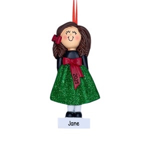 May include: A green glitter Christmas ornament with a brown haired girl wearing a black dress and a red bow. The ornament has the year 2025 and the name Jane on it.