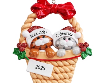 May include: A Christmas ornament featuring two kittens wearing Santa hats in a basket with the names "Alexander" and "Catherine" and the year "2025" on a tag.