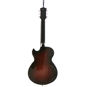 May include: A decorative guitar ornament with a glossy, two-tone finish. The body transitions from a dark brown to a lighter brown, with a black neck and headstock. A black string is attached for hanging.