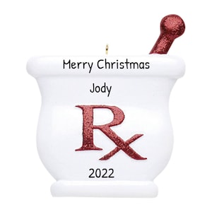 May include: White ceramic mortar and pestle Christmas ornament with red glitter "Rx" and the text "Merry Christmas Jody 2022".