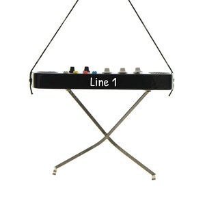 May include: A black electronic device with the text "Line 1" on the front, supported by a silver metal stand. The device has several colored buttons and knobs on top and is suspended by a black string.