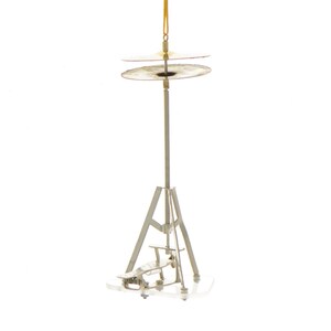 Op de afbeelding: Een zilveren metalen ornament in de vorm van een bekkenstel met twee bekkens. De ornament is opgehangen aan een gouden touwtje.