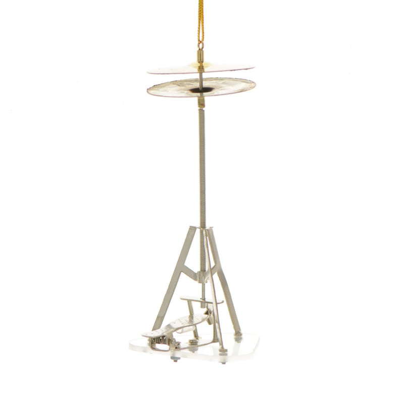 Op de afbeelding: Een zilveren metalen ornament in de vorm van een bekkenstel met twee bekkens. De ornament is opgehangen aan een gouden touwtje.