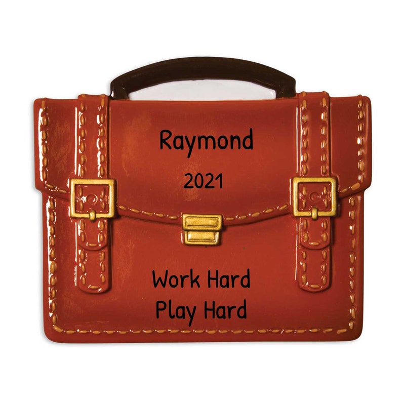 May include: A red leather briefcase ornament with gold accents and the text "Raymond 2021 Work Hard Play Hard".