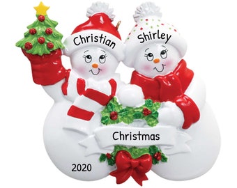 May include: A white snowman couple Christmas ornament with red and white striped scarves, red hats, and a green holly wreath. The ornament has the names "Christian" and "Shirley" and the text "Christmas 2020".