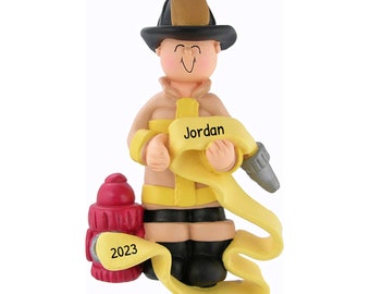 Può includere: Un ornamento natalizio personalizzato con un vigile del fuoco dei cartoni animati che tiene un tubo antincendio giallo. L'ornamento è decorato con un idrante rosso e il nome "Jordan" è scritto sul tubo. L'anno "2023" è stampato sull'idrante.