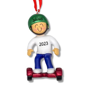 May include: A green and white personalized Christmas ornament of a person riding a self-balancing scooter. The ornament has the name "Julius" and the year "2023" on it.