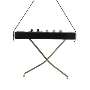 May include: A miniature black synthesizer with colorful knobs and buttons, suspended by a black string. It rests on a silver, X-shaped stand. The synthesizer has a sleek, glossy finish and a minimalist design, perfect for music enthusiasts.