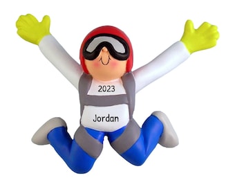 Può includere: Un ornamento da appendere a forma di paracadutista con un casco rosso, una tuta bianca e pantaloni blu. L'ornamento ha il testo "2023" e "Jordan" su di esso.