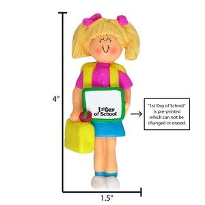 May include: A 4-inch tall girl figurine ornament with blonde hair, wearing a pink shirt, yellow vest, blue skirt, and white shoes. She is holding a green book that says "1st Day of School" and a yellow lunchbox. The text "1st Day of School" is pre-printed and cannot be changed or erased.
