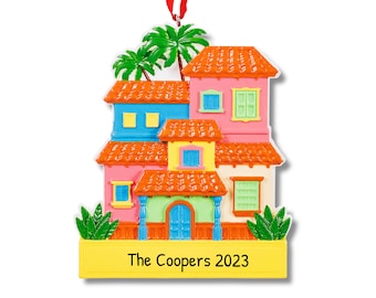 Puede incluir: Un adorno de casa colorido de varios niveles con una cinta roja para colgar. La casa tiene un exterior amarillo, verde, azul y rosa con techos de tejas naranjas. Se pueden ver palmeras detrás de la casa. El adorno tiene una pancarta amarilla con el texto "The Coopers 2023".