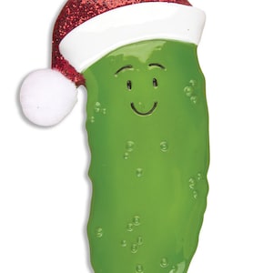 Puede incluir: Un adorno de Navidad de pepinillo verde con un gorro de Pap&aacute; Noel rojo y blanco. El pepinillo tiene una cara sonriente y est&aacute; decorado con puntos blancos.