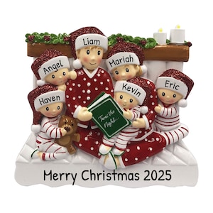 May include: A Christmas ornament featuring a family of five in red and white pajamas, reading a book titled "Twas the Night..." by the fireplace. The ornament is white with the text "Merry Christmas 2025" at the bottom.