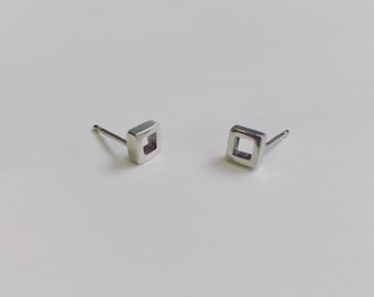 May include: A pair of silver square stud earrings with a hollow center.