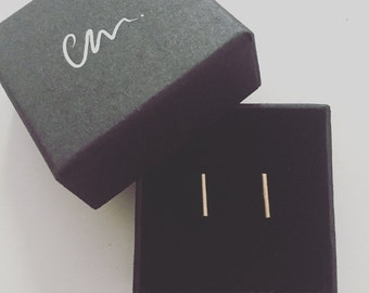 May include: A pair of gold bar earrings in a black jewelry box. The box has the word "cm." written on the top.