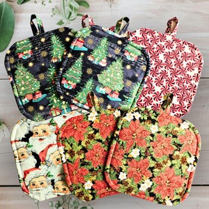 May include: Five square quilted pot holders featuring holiday patterns including decorated Christmas trees on black, red and white peppermint swirls, vintage Santa Claus faces, and red poinsettia flowers with green leaves and pinecones.