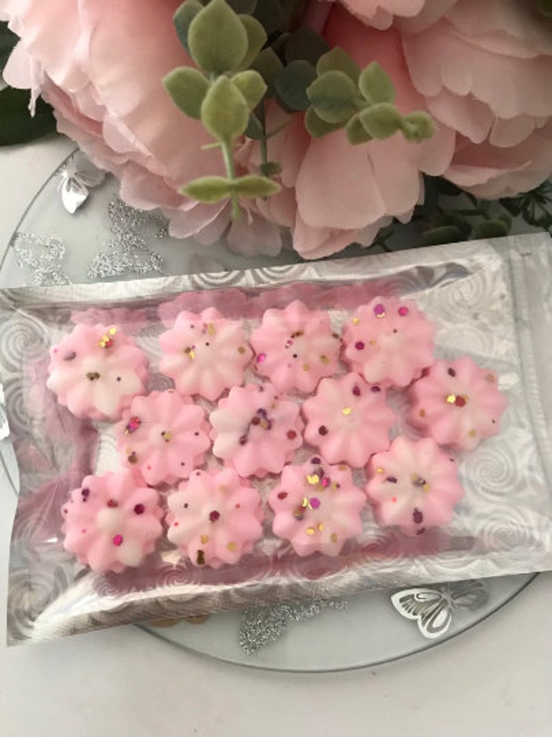 K&ouml;nnte beinhalten: Nahaufnahme einer Packung rosa Wachs-Schmelzen in Form von Blumen. Die Wachs-Schmelzen sind mit Glitzer verziert und in einer durchsichtigen Plastikt&uuml;te verpackt.