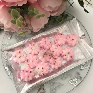 K&ouml;nnte beinhalten: Nahaufnahme einer Packung rosa Wachs-Schmelzen in Form von Blumen. Die Wachsschmelzen sind mit Glitzer verziert und befinden sich in einem durchsichtigen Plastikbeutel.