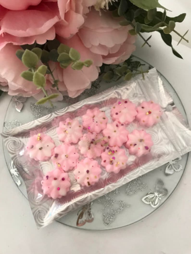 K&ouml;nnte beinhalten: Nahaufnahme einer Packung rosa Wachs-Schmelzen in Form von Blumen. Die Wachsschmelzen sind mit Glitzer verziert und befinden sich in einem durchsichtigen Plastikbeutel.