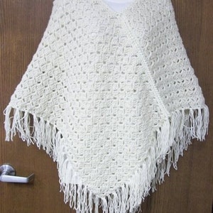 May include: White crocheted poncho with fringe trim.